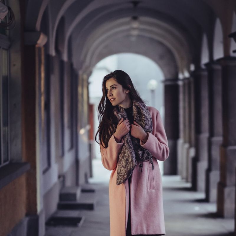 Model im rosa Mantel mit Paisley-Schal unter einer steinernen Arkade