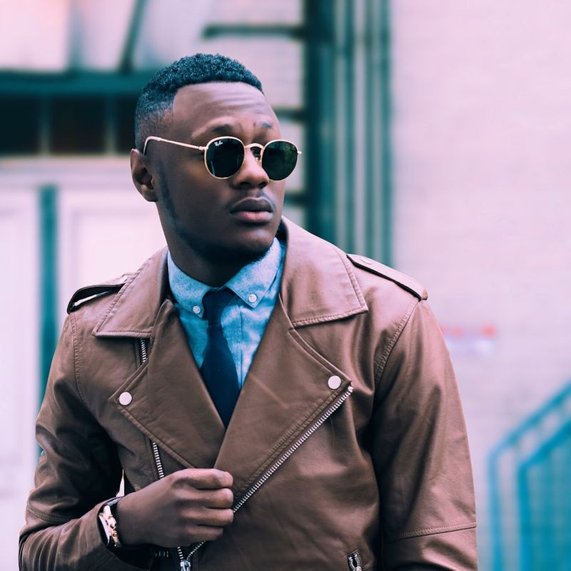 Model im braunen Trenchcoat mit blauem Hemd, Krawatte und runder Sonnenbrille